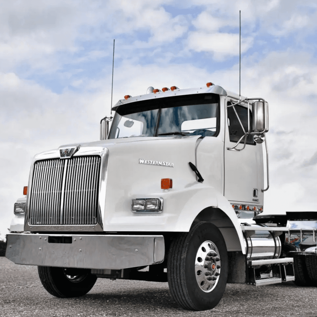 A white Western Star semi‑truck is parked on a gravel lot under a cloudy sky.