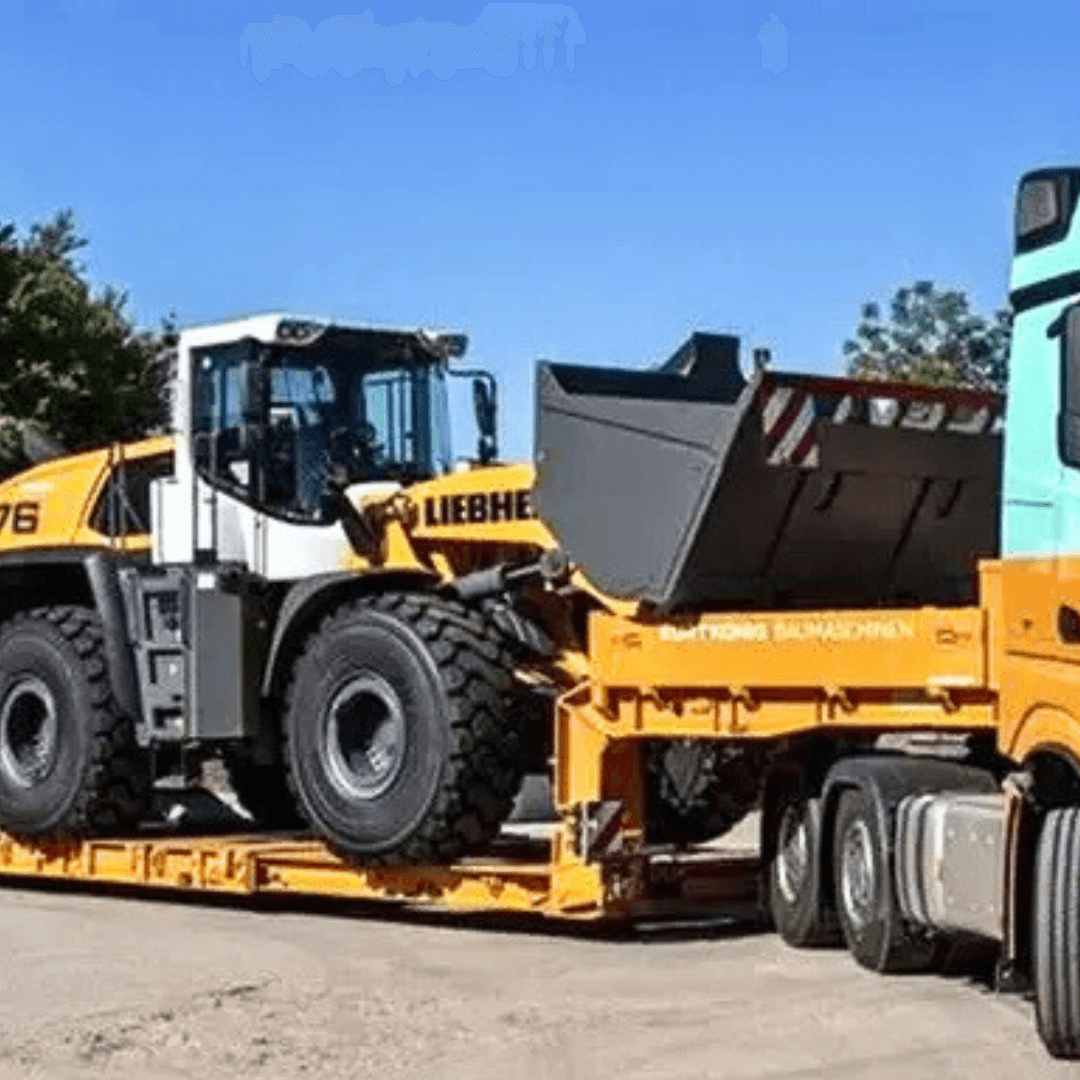 A large yellow Liebherr wheel loader is loaded onto an orange construction trailer pulled by a truck, parked on a dirt lot under a clear blue sky