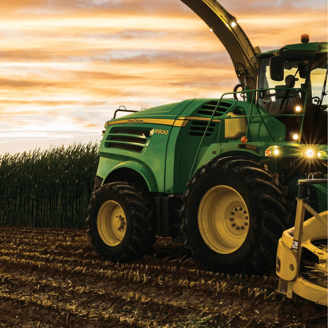 An image of a green John deere tractor in a field pulling a plow with the sunset in the background