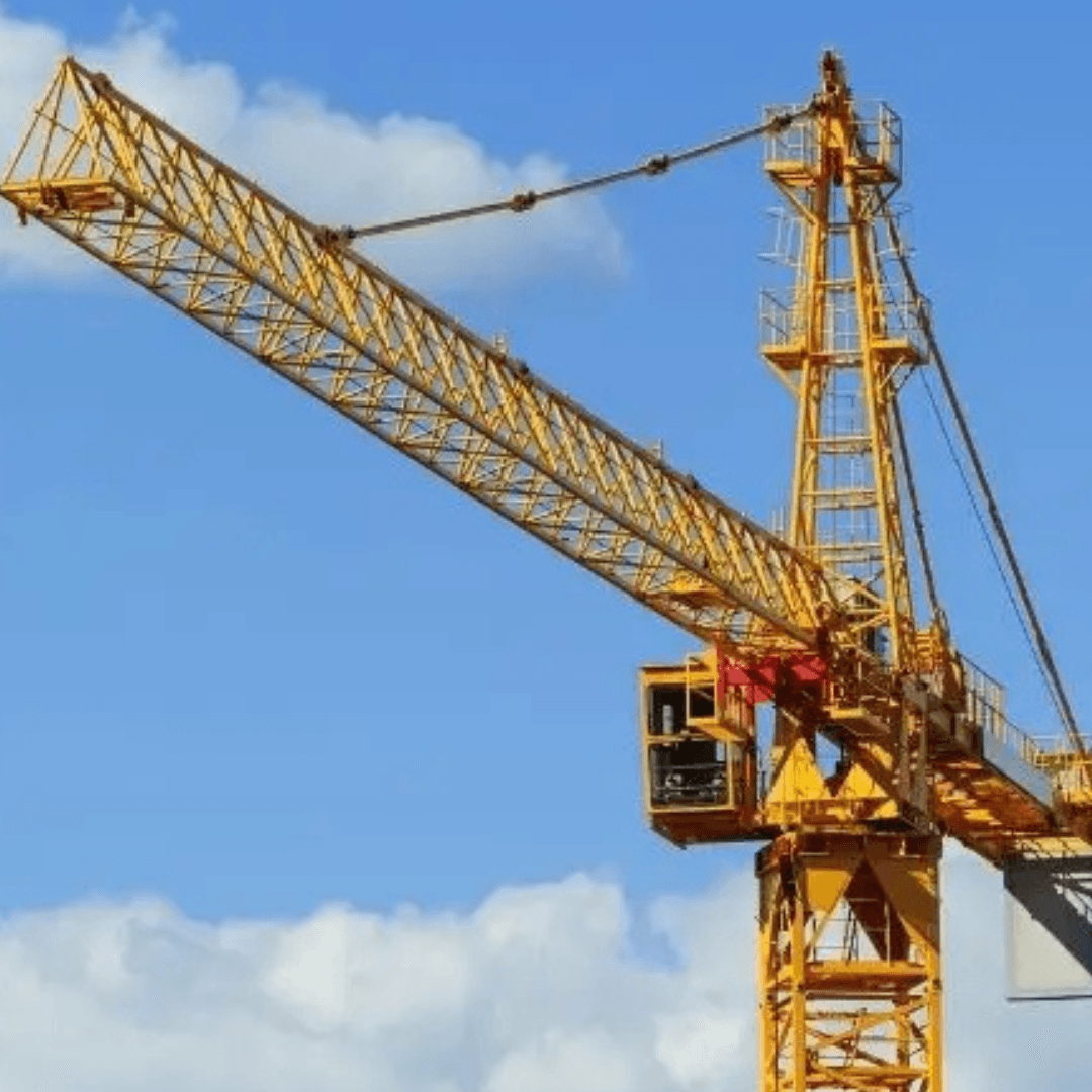 A tall yellow tower crane with a long horizontal jib is shown against a blue sky with clouds, with the operator cab visible near the base of the jib