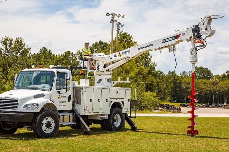 Utility truck with a raised bucket lift and a worker in safety gear operating it outdoors.
