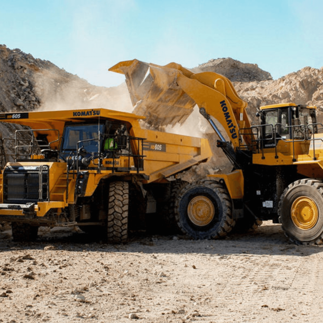 An image of a Komatsu wheel loader dumping dirt in the bed of a Komatsu articulated dump truck in a rock quarry on a sunny day