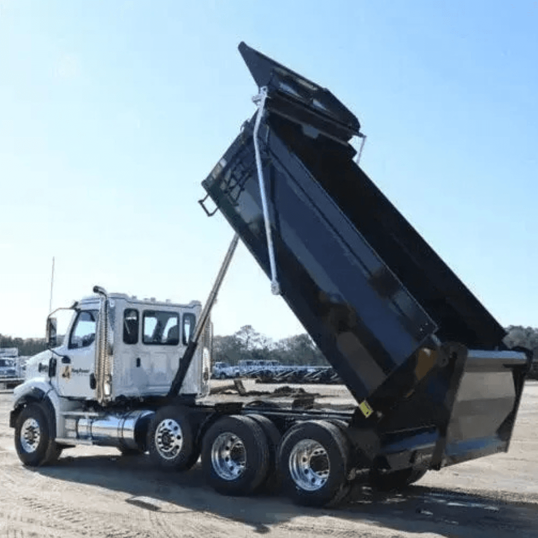 A white dump truck with a raised black dump bed is parked on a dirt lot under a clear sky.