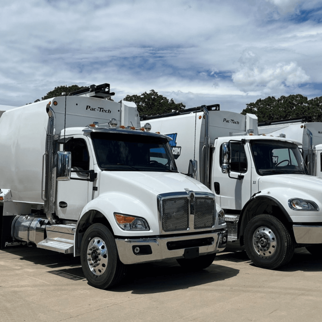 An image of white drump trucks parked in a parking lot under a partly cloudy sky
