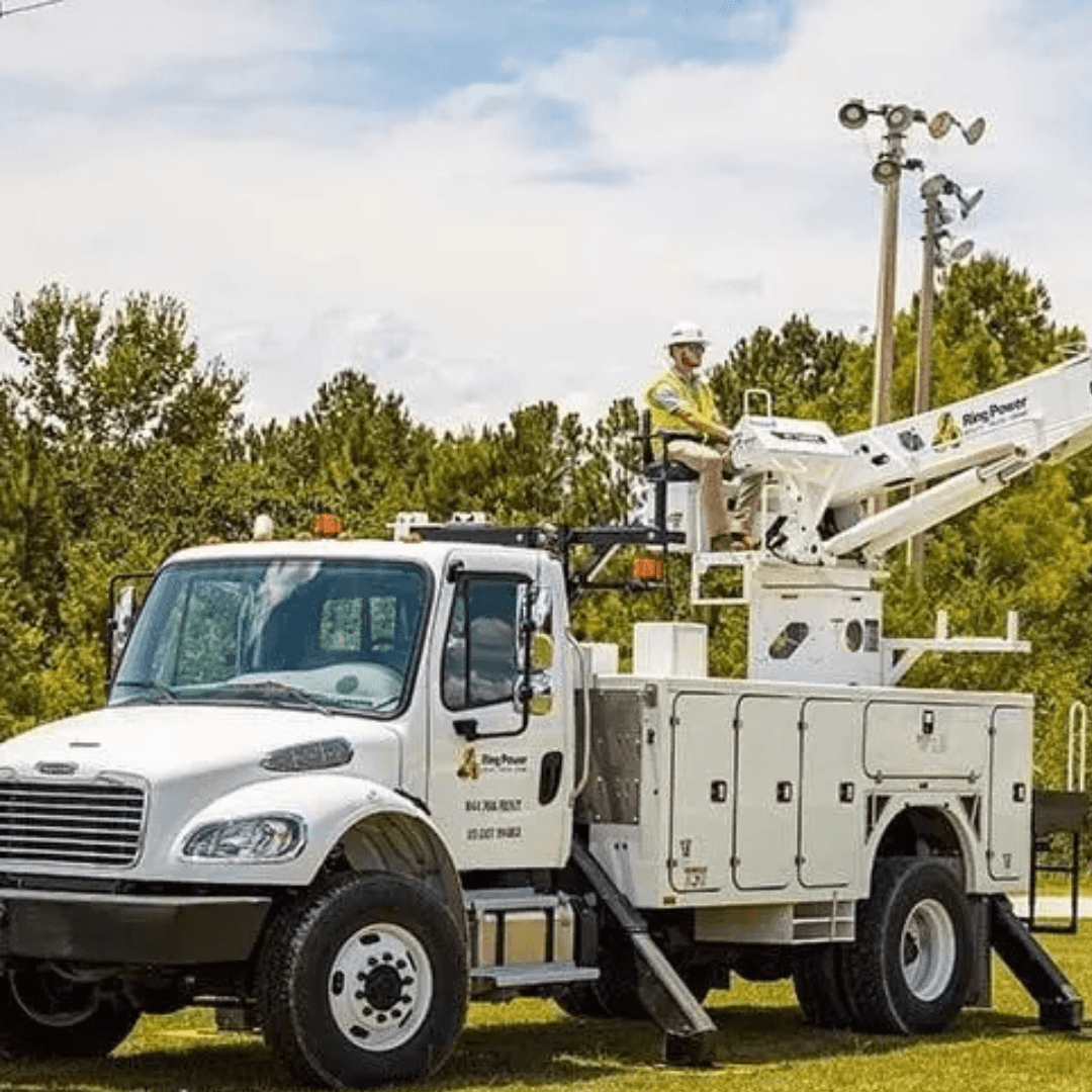 Utility truck with a raised bucket lift and a worker in safety gear operating it outdoors.